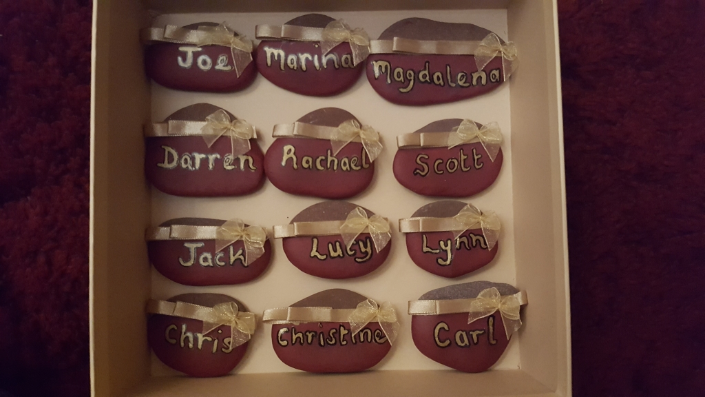 Hand painted red smooth pebbles with wedding guest names, bows and ribbons in gold